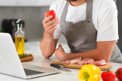 Photo of Man making dinner while watching online cooking course via laptop in kitchen, closeup