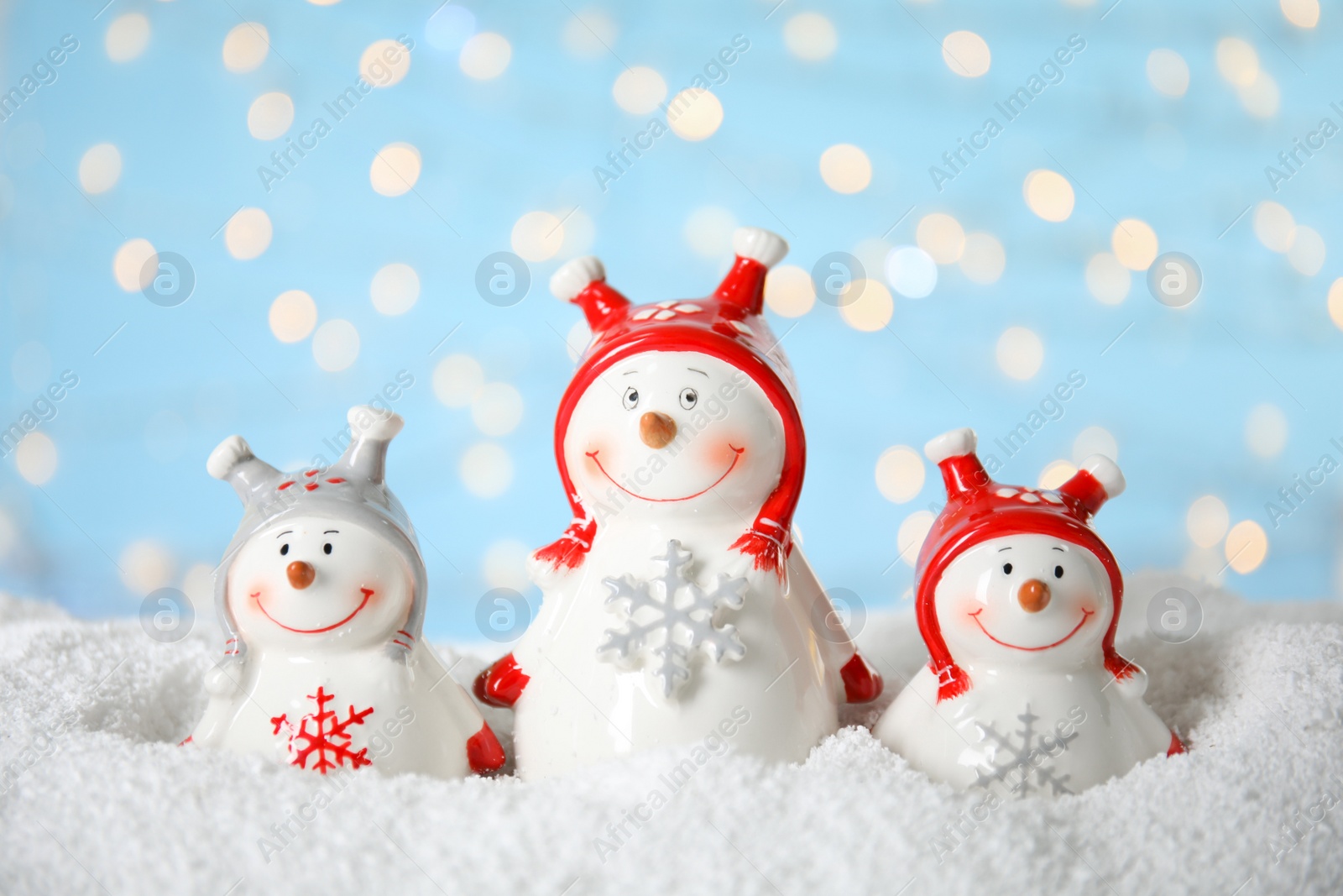 Photo of Decorative snowmen on artificial snow against blurred festive lights