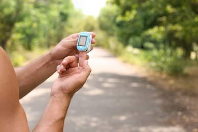 Young man checking pulse with medical device in park, closeup. Space for text
