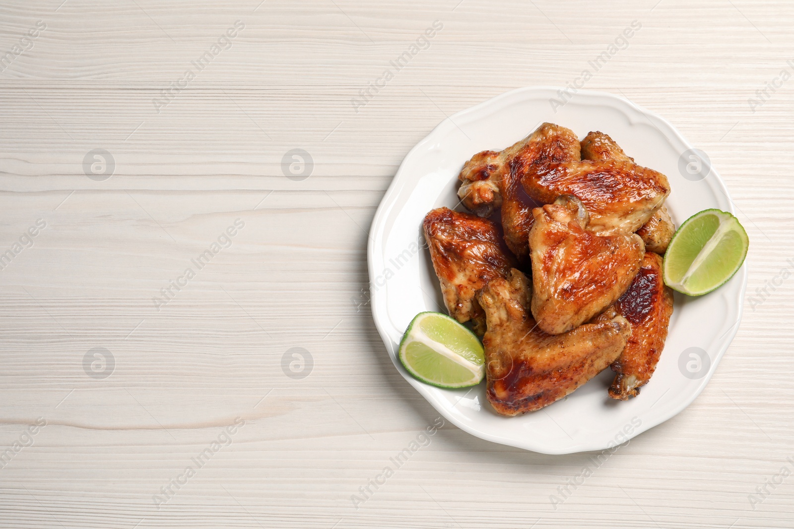 Photo of Plate with delicious fried chicken wings and lime on white wooden table, top view. Space for text