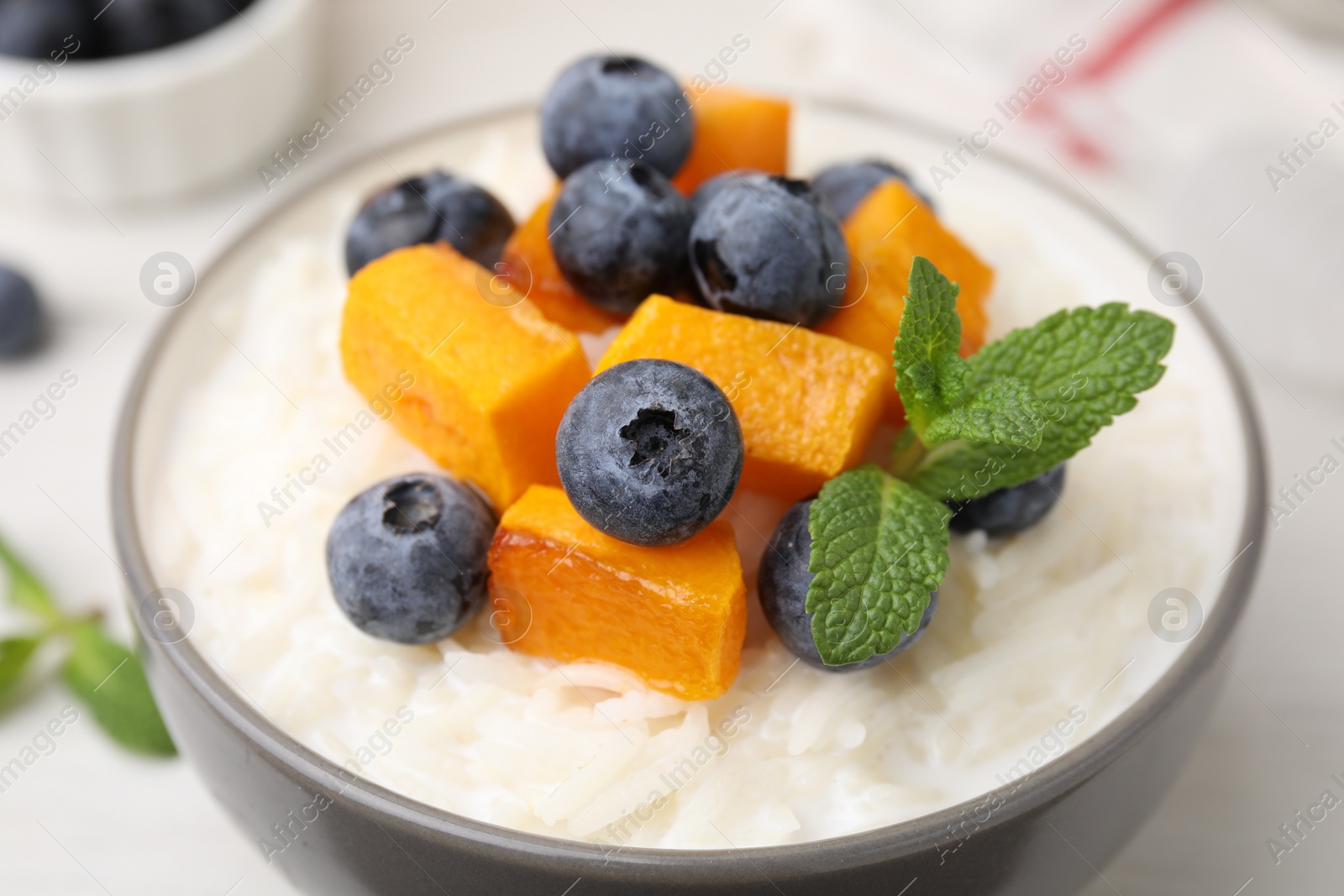 Photo of Bowl of delicious rice porridge with blueberries, pumpkin and mint on table, closeup