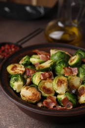 Photo of Delicious roasted Brussels sprouts and bacon in bowl on brown table, closeup