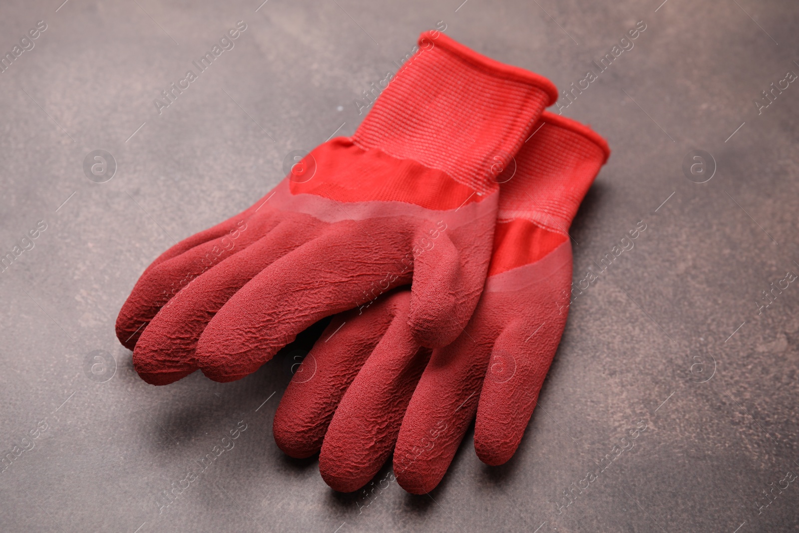 Photo of Pair of red gardening gloves on brown textured table