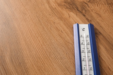 Photo of Weather thermometer on wooden table, closeup. Space for text