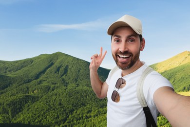 Smiling man taking selfie and showing peace sign in mountains