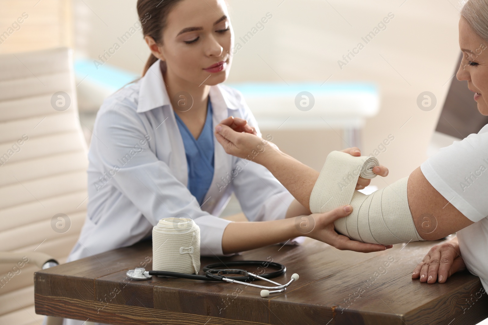 Photo of Female orthopedist applying bandage onto patient's elbow in clinic, closeup