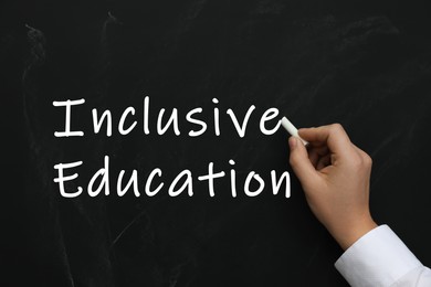 Woman writing phrase INCLUSIVE EDUCATION on blackboard, closeup