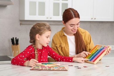 Happy mother and daughter playing with different math game kits at white marble table in kitchen. Learning mathematics with fun