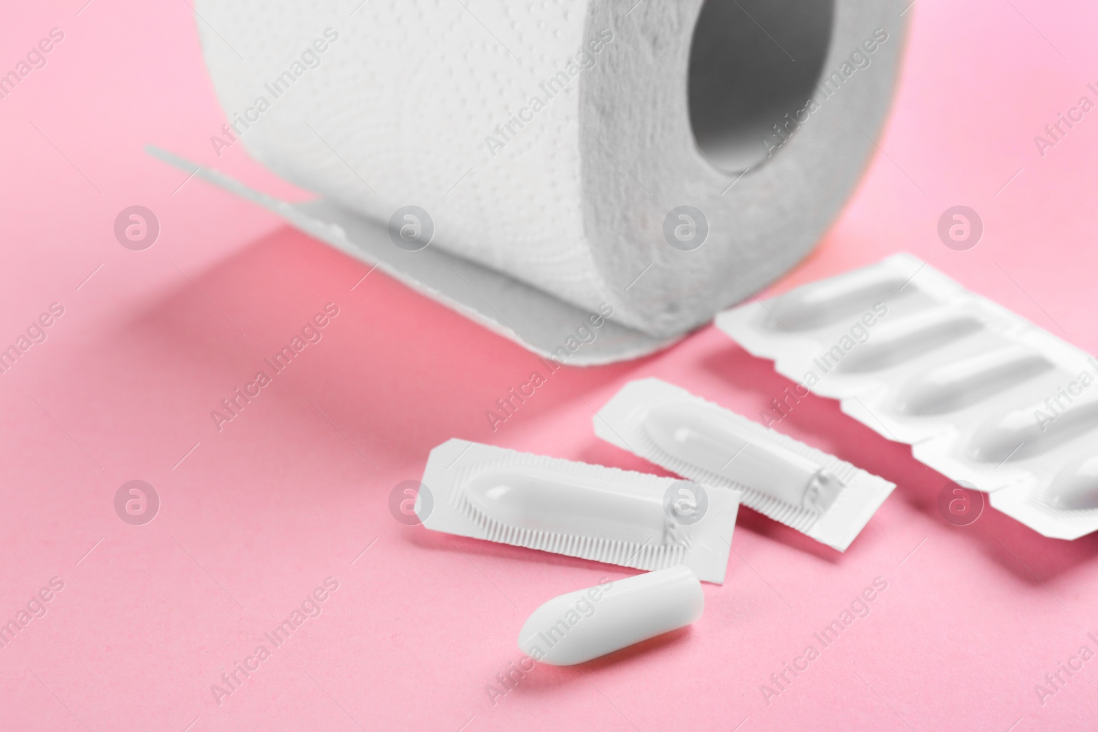 Photo of Suppositories and toilet paper on pink background, closeup view. Hemorrhoid treatment