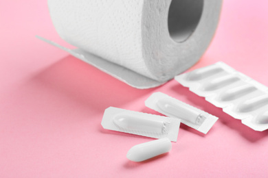 Suppositories and toilet paper on pink background, closeup view. Hemorrhoid treatment
