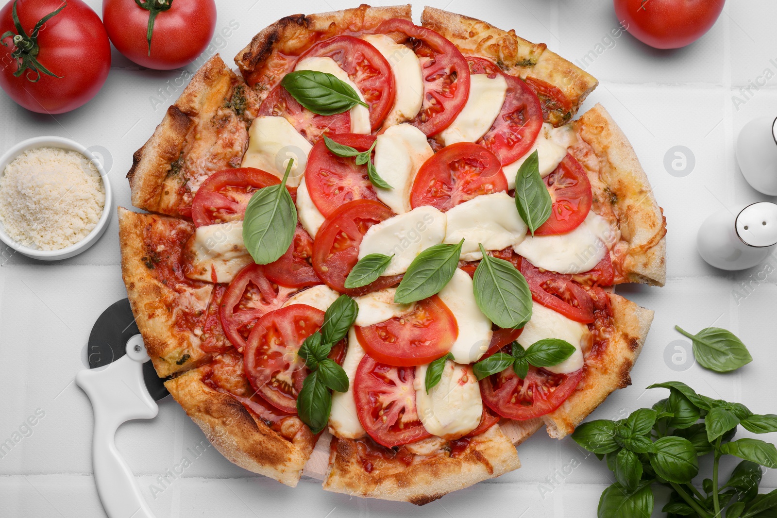 Photo of Delicious Caprese pizza with tomatoes, mozzarella and basil on white tiled table, flat lay