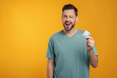 Photo of Excited man holding condom on orange background. Space for text