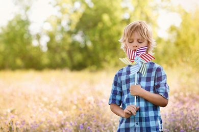 Photo of Cute little boy with pinwheel outdoors, space for text. Child spending time in nature