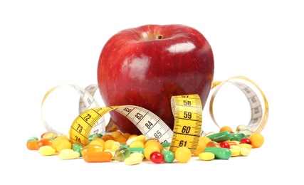 Weight loss pills, apple and measuring tape on white background