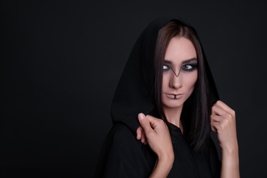 Mysterious witch in mantle with hood on black background. Space for text