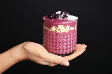 Photo of Woman holding glass with tasty acai smoothie on black background