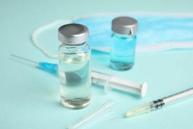 Photo of Vials, syringes and surgical mask on turquoise  background. Vaccination and immunization