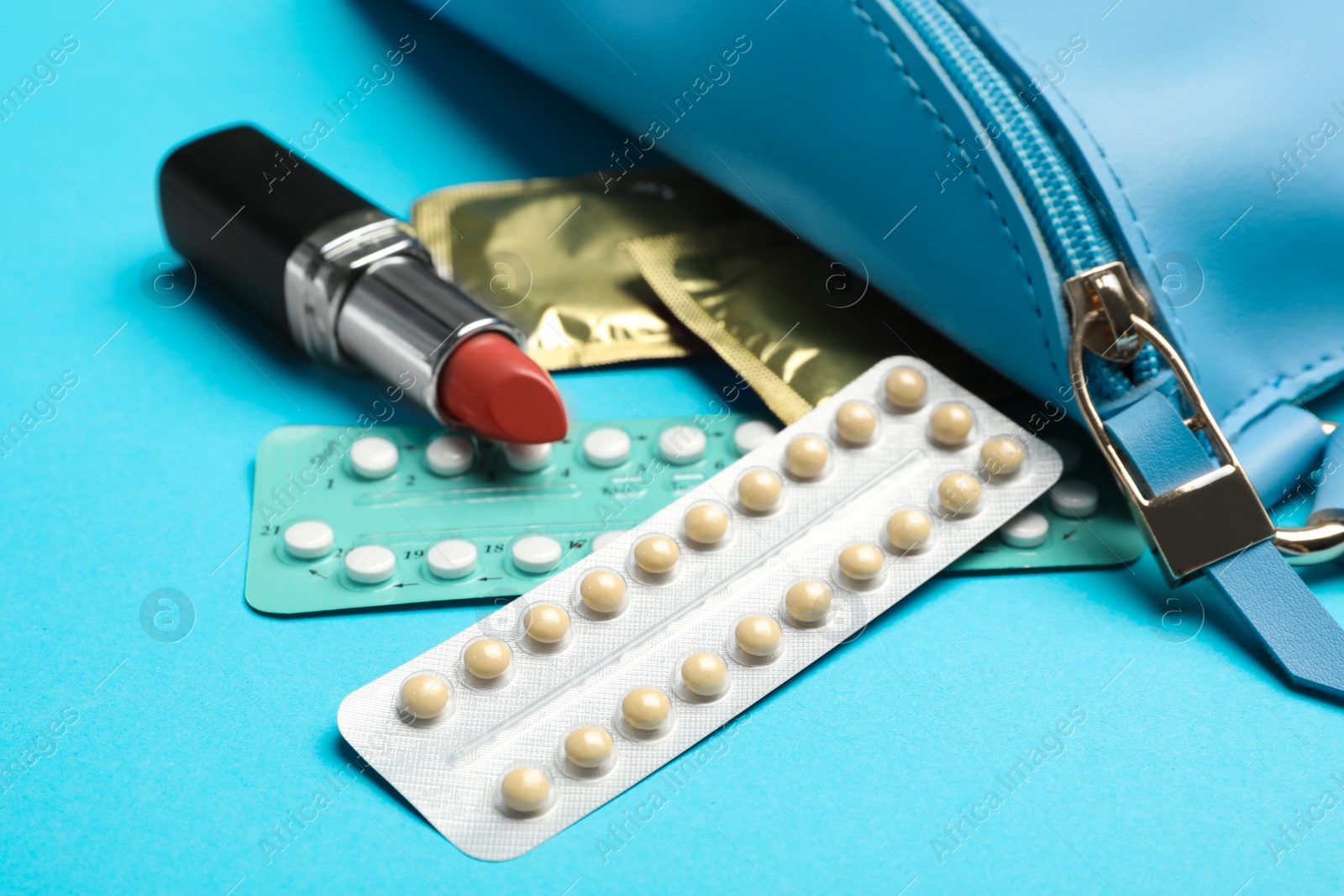 Photo of Different contraceptives and red lipstick near bag on light blue background. Safe sex concept