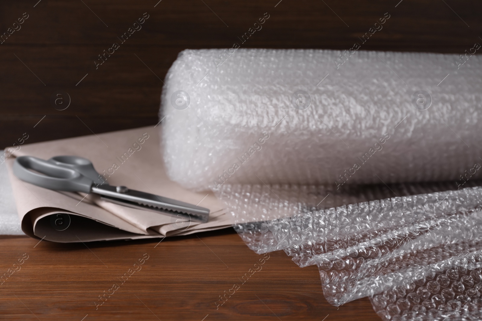 Photo of Scissors, paper and roll of bubble wrap on wooden table