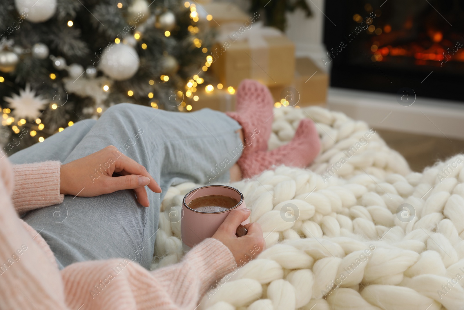 Photo of Woman with cup of hot drink resting near fireplace  in living room decorated for Christmas, closeup