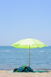 Photo of Light green beach umbrella in sand near sea on sunny day