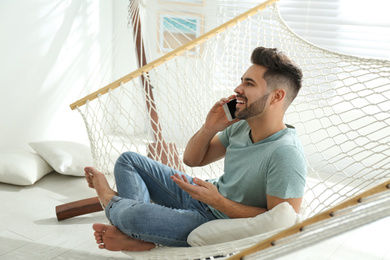 Photo of Young man talking on mobile phone in hammock at home