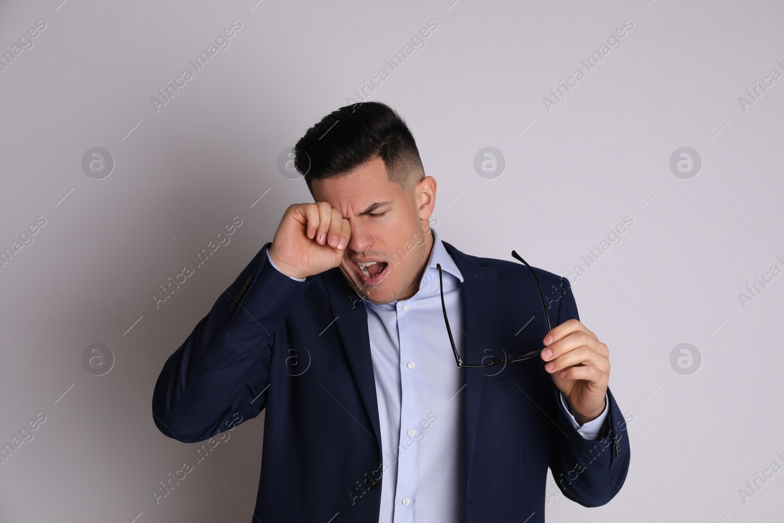 Photo of Handsome tired businessman yawning on light grey background