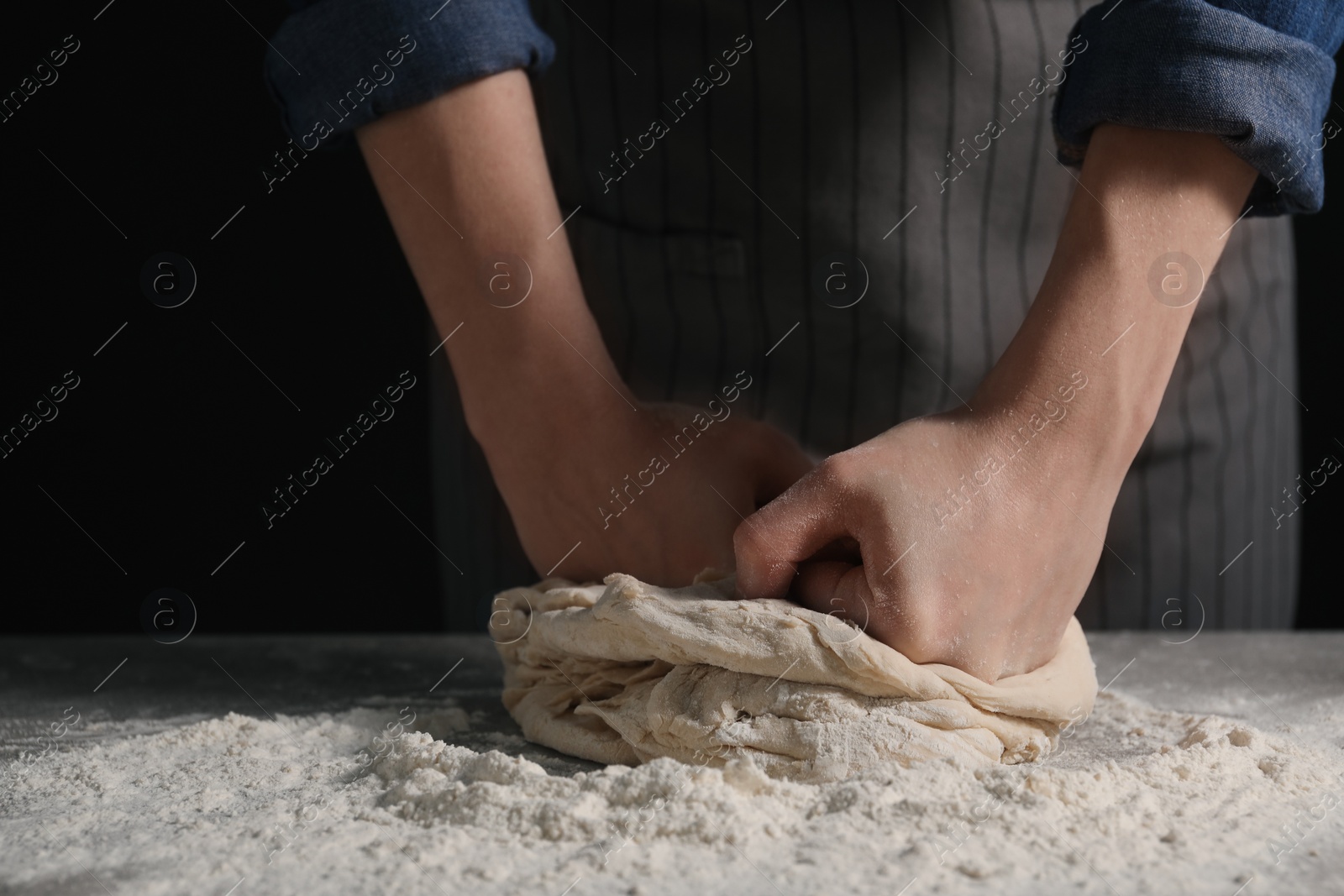 Photo of Making bread. Woman kneading dough at table on dark background, closeup