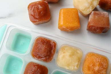 Photo of Different fruit puree in ice cube tray on white table, flat lay