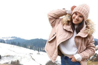 Photo of Young woman in warm clothes near snowy hill, space for text. Winter vacation