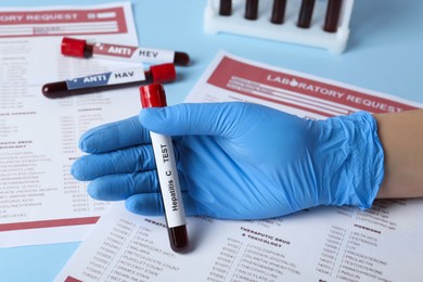 Photo of Scientist holding tube with blood sample and label Hepatitis C test near laboratory form, closeup