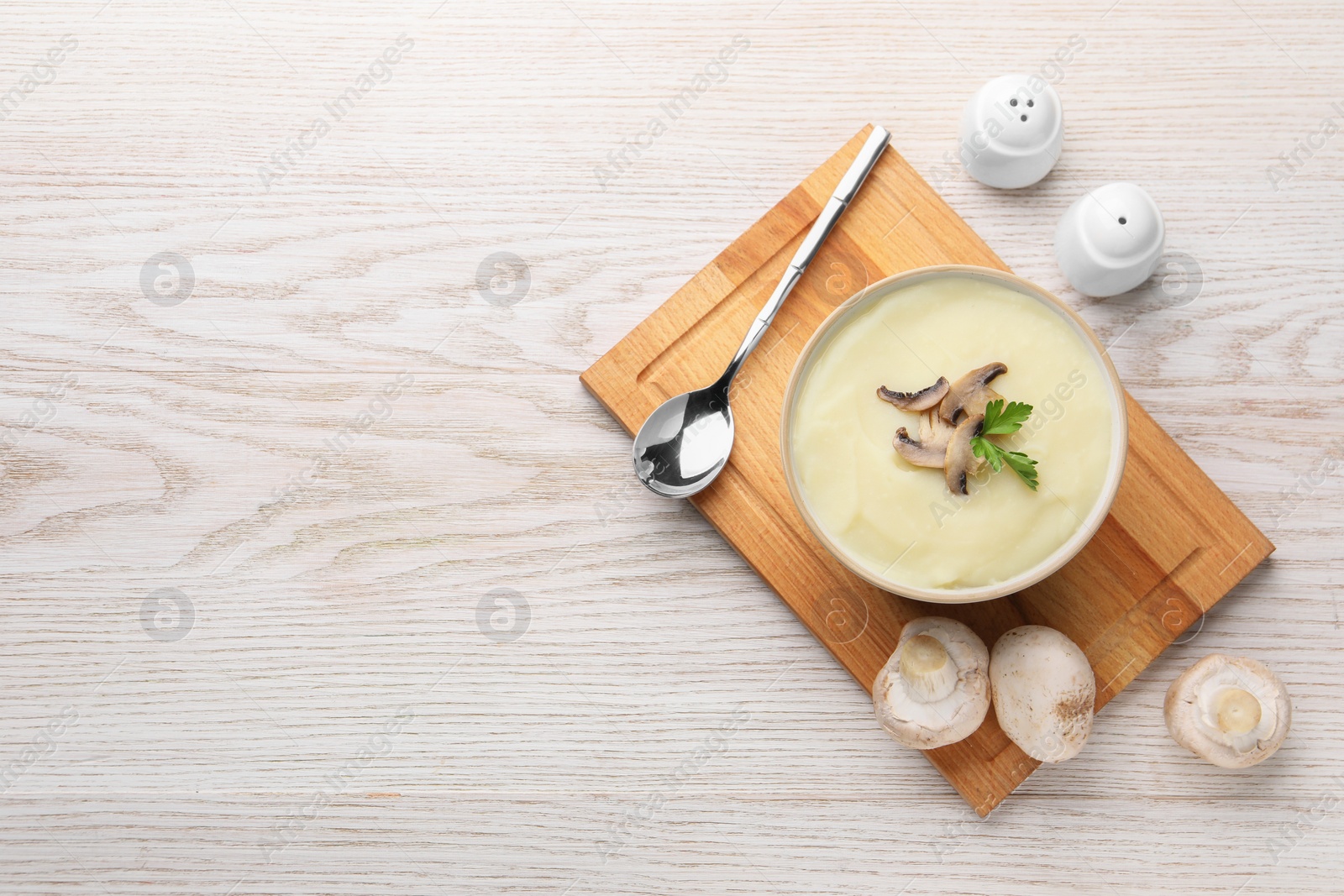 Photo of Bowl of tasty cream soup with mushrooms, parsley and spoon on light wooden table, flat lay. Space for text