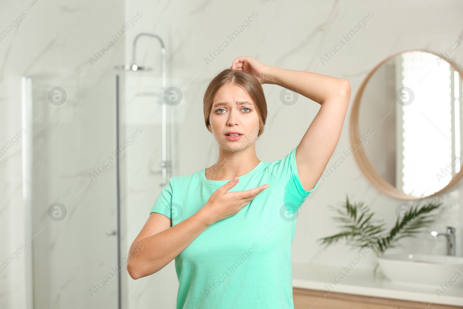 Photo of Young woman with sweat stain on her clothes in bathroom. Using deodorant
