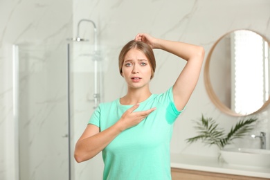 Young woman with sweat stain on her clothes in bathroom. Using deodorant