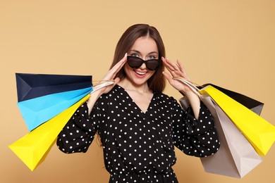 Stylish young woman in sunglasses with shopping bags on beige background