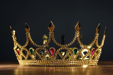 Photo of Beautiful golden crown with gems on wooden table. Fantasy item