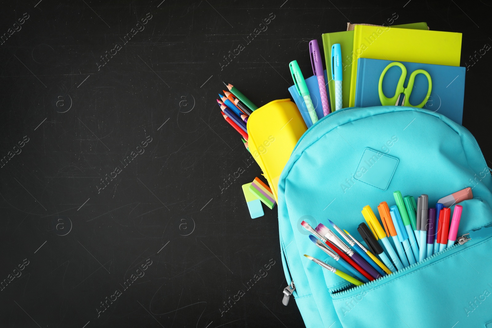 Photo of Light blue backpack with different stationery on blackboard, top view and space for text. Back to school