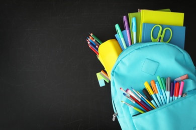 Light blue backpack with different stationery on blackboard, top view and space for text. Back to school