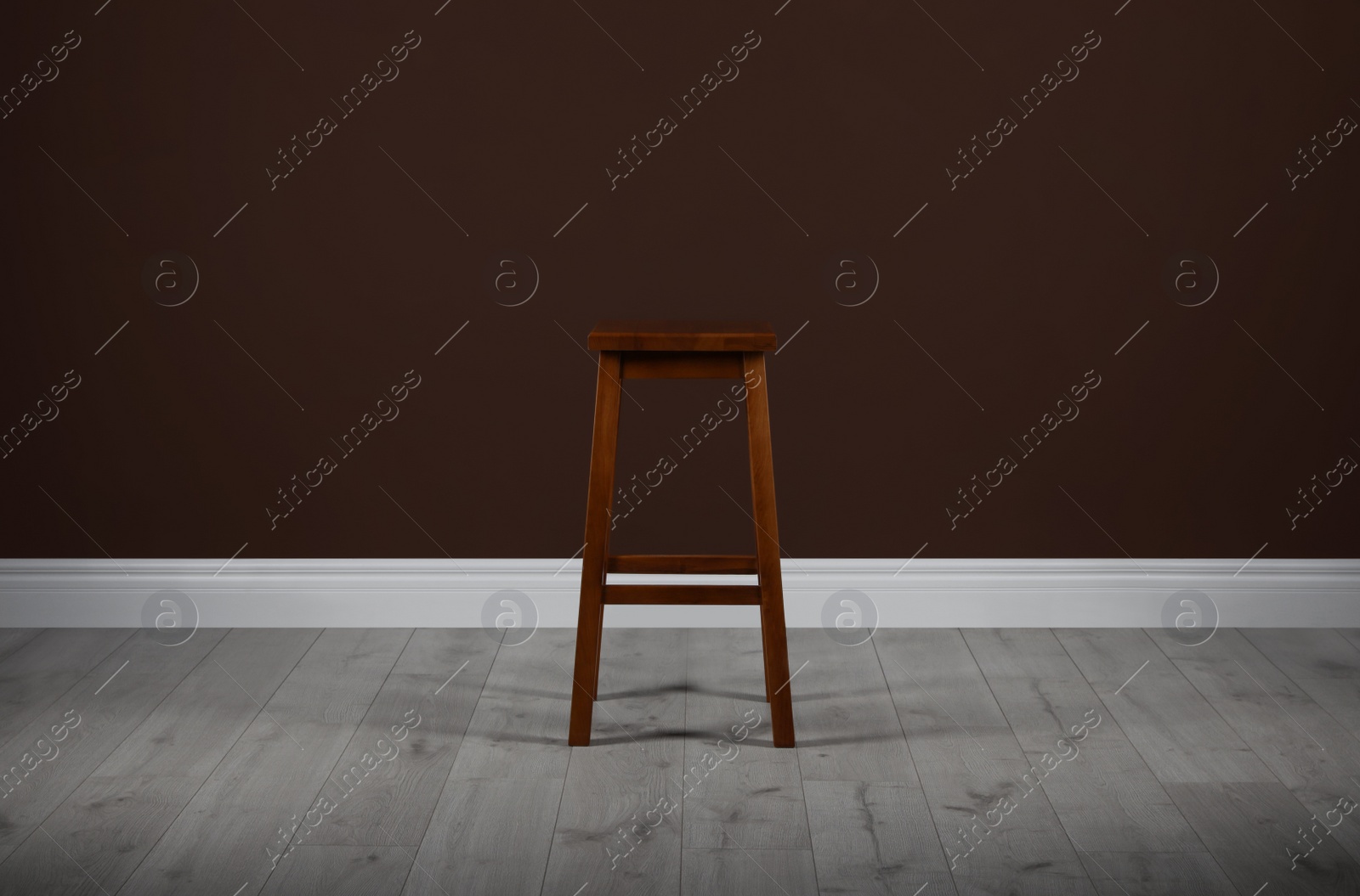 Photo of Stylish wooden stool near brown wall indoors