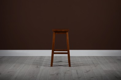 Photo of Stylish wooden stool near brown wall indoors