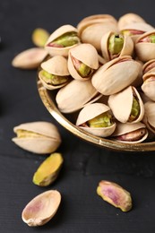Photo of Tasty pistachios in bowl on black table, closeup