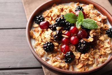 Photo of Bowl of muesli served with berries and milk on wooden table, closeup