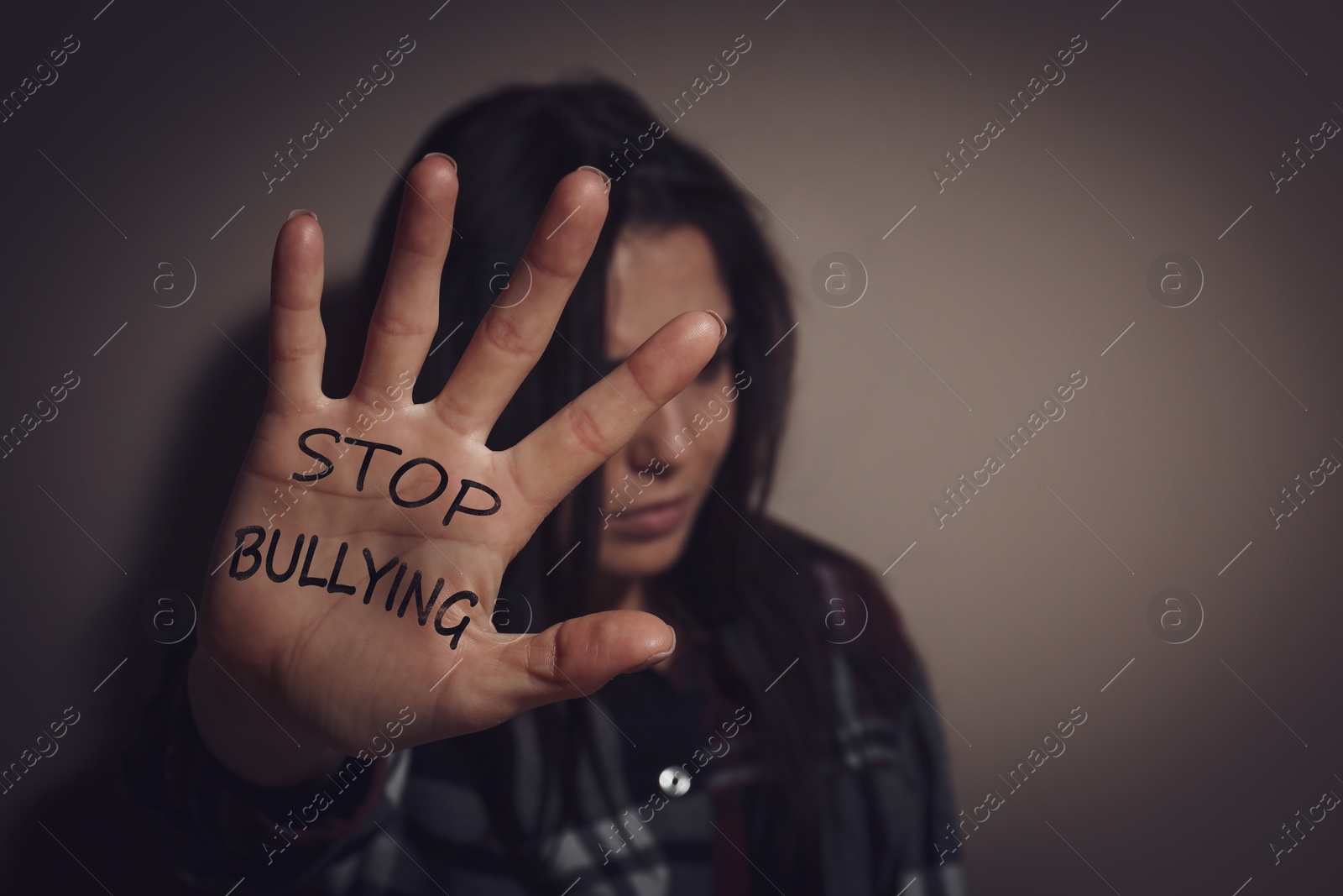 Image of Abused teen girl showing palm with message STOP BULLYING near beige wall, focus on hand