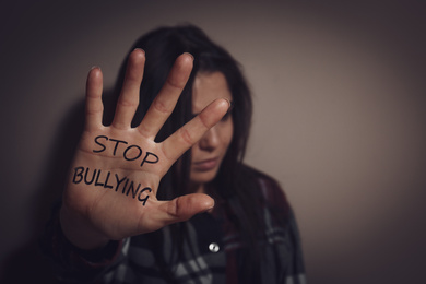 Image of Abused teen girl showing palm with message STOP BULLYING near beige wall, focus on hand