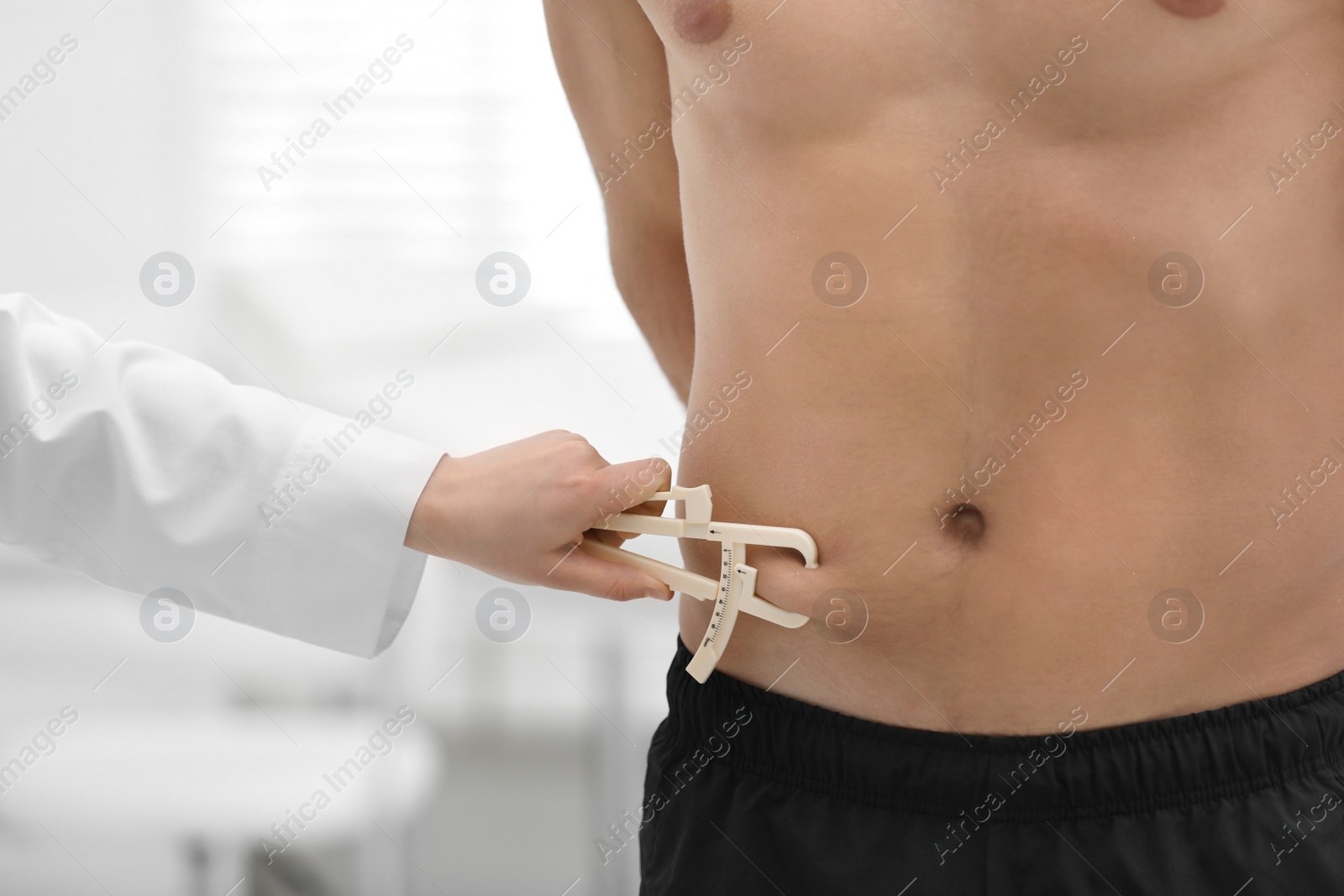 Photo of Nutritionist measuring man's body fat layer with caliper on blurred background, closeup