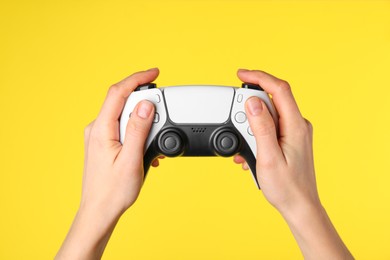 Woman using game controller on yellow background, closeup