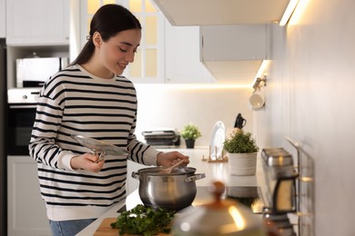 Photo of Smiling woman with spoon and lid cooking soup in kitchen