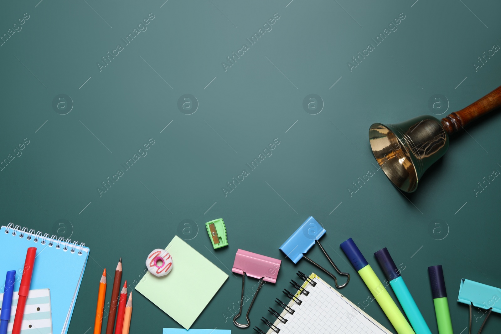 Photo of Flat lay composition with golden bell and school stationery on green chalkboard, space for text