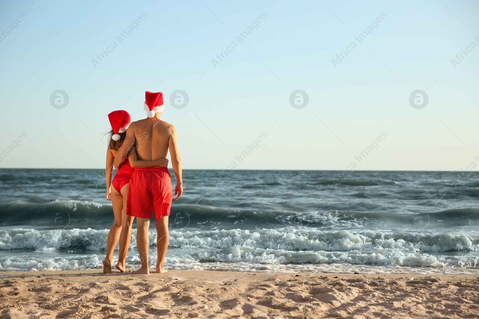 Photo of Lovely couple with Santa hats together on beach, back view. Christmas vacation