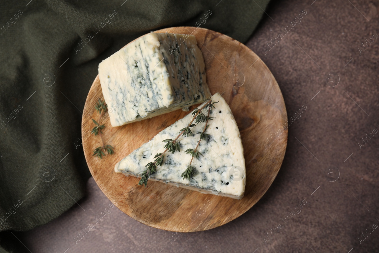 Photo of Tasty blue cheese with thyme on brown table, top view